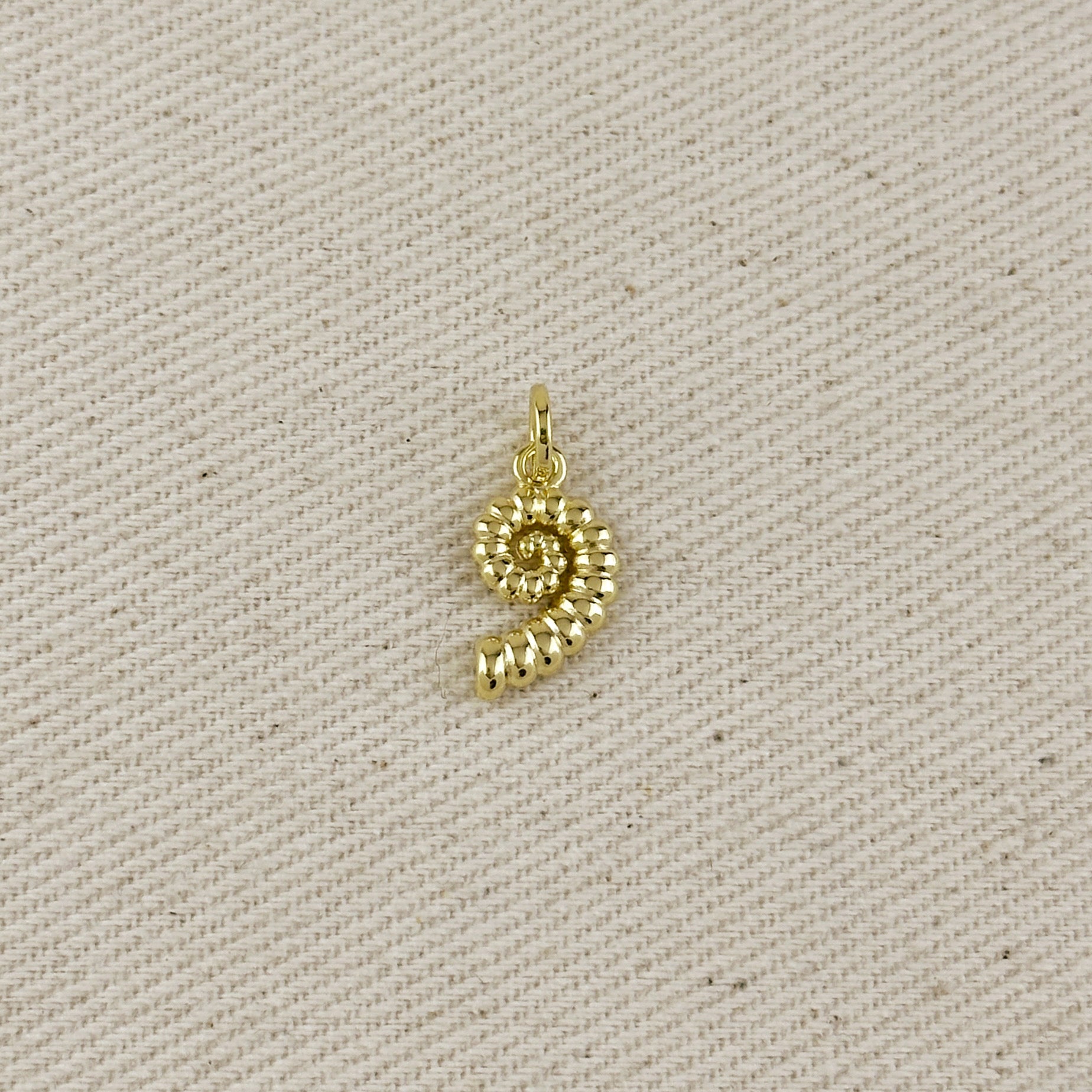 Gold spiral pendant on a beige fabric background