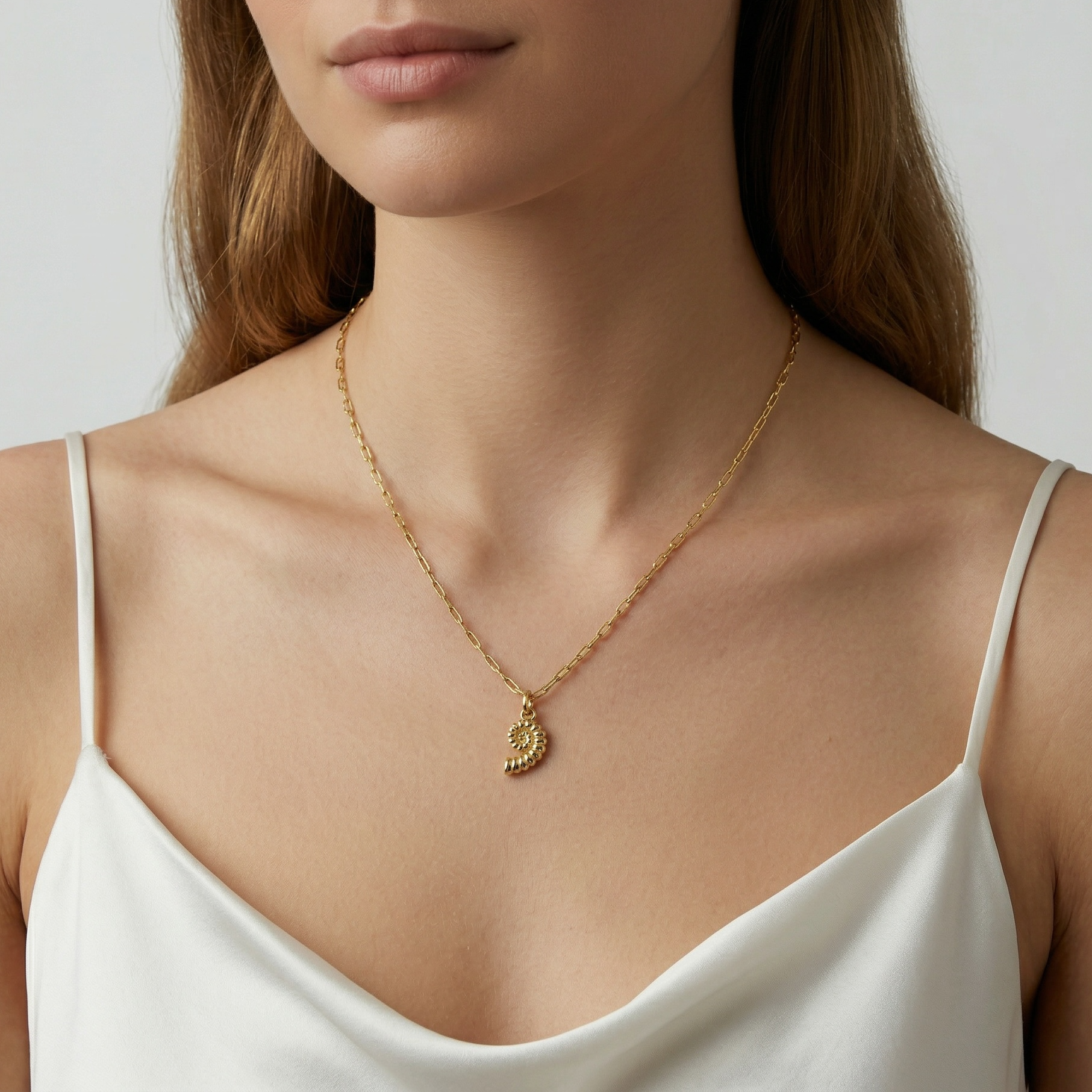 Woman wearing a gold necklace with a sundial shell pendant on a plain background