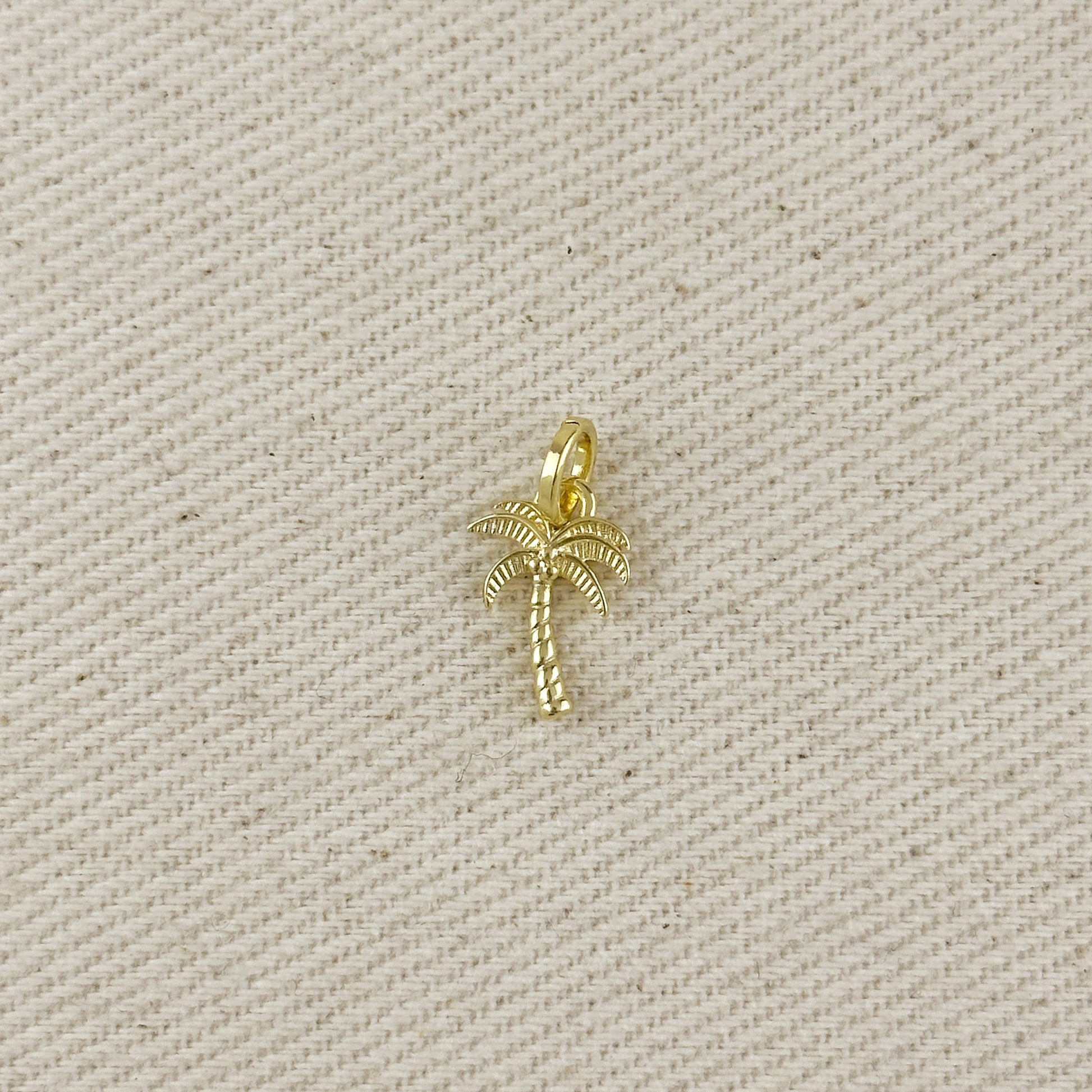 Gold palm tree charm on a beige fabric background