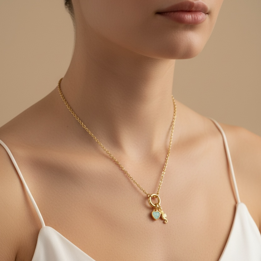 Gold necklace with a heart pendant worn by a person in a white top against a beige background