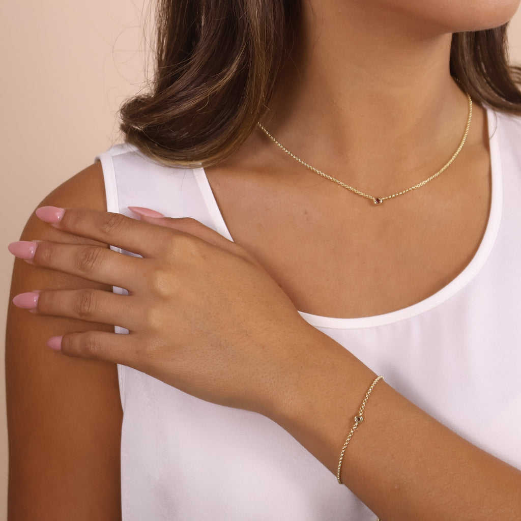 Woman wearing a gold necklace and bracelet on a beige background