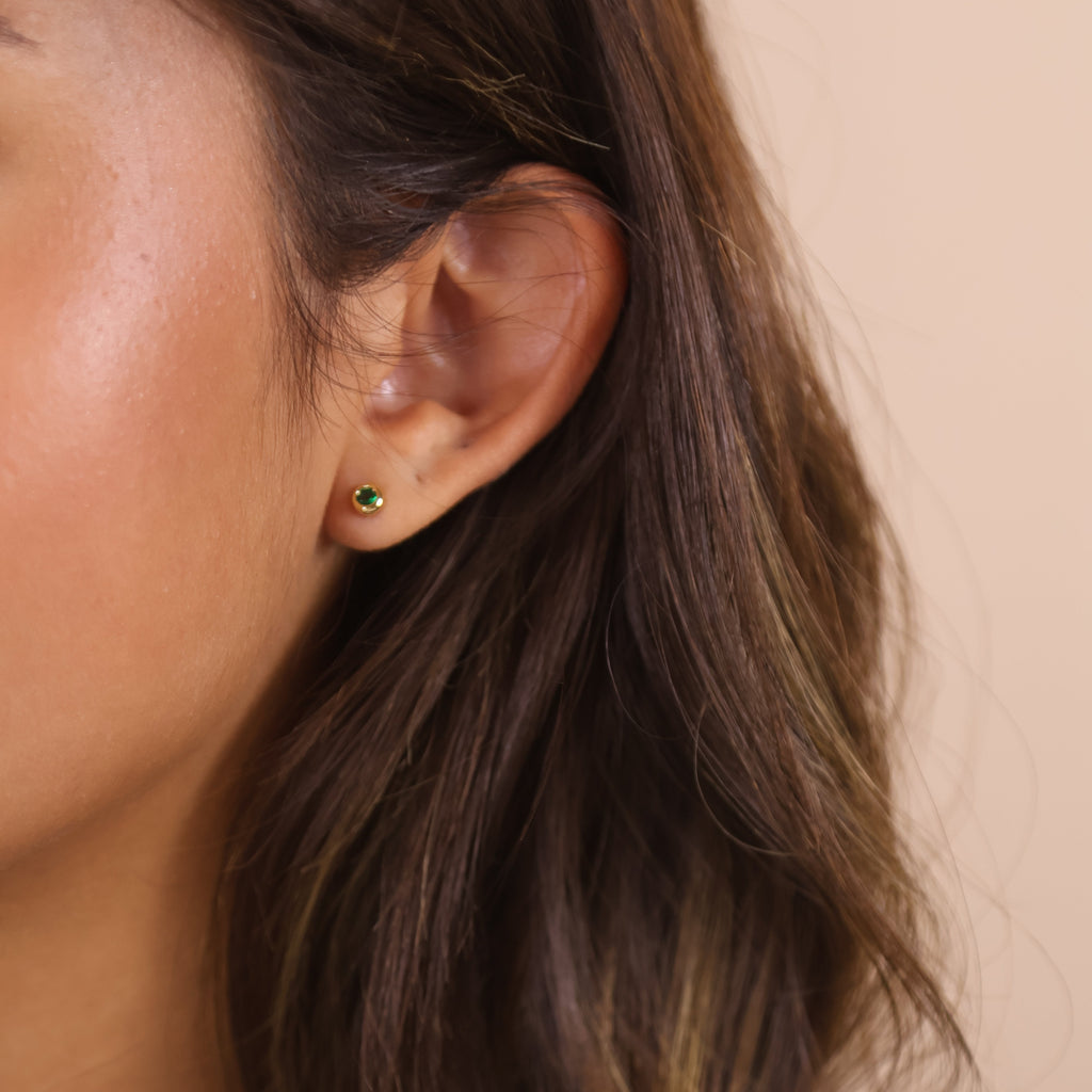 Model showcasing 18K gold filled dainty bezel CZ birthstone stud earrings in green.