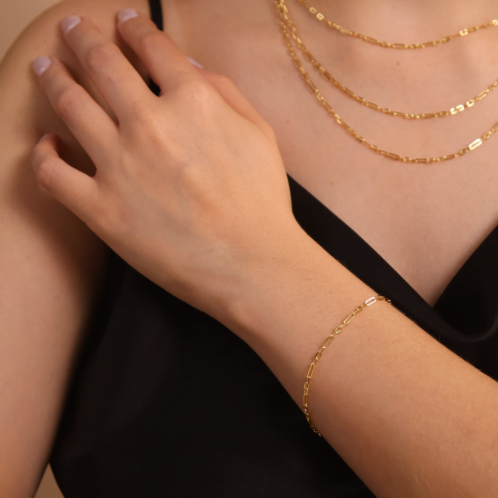 Close-up of a person wearing gold necklaces and bracelets on a neutral background