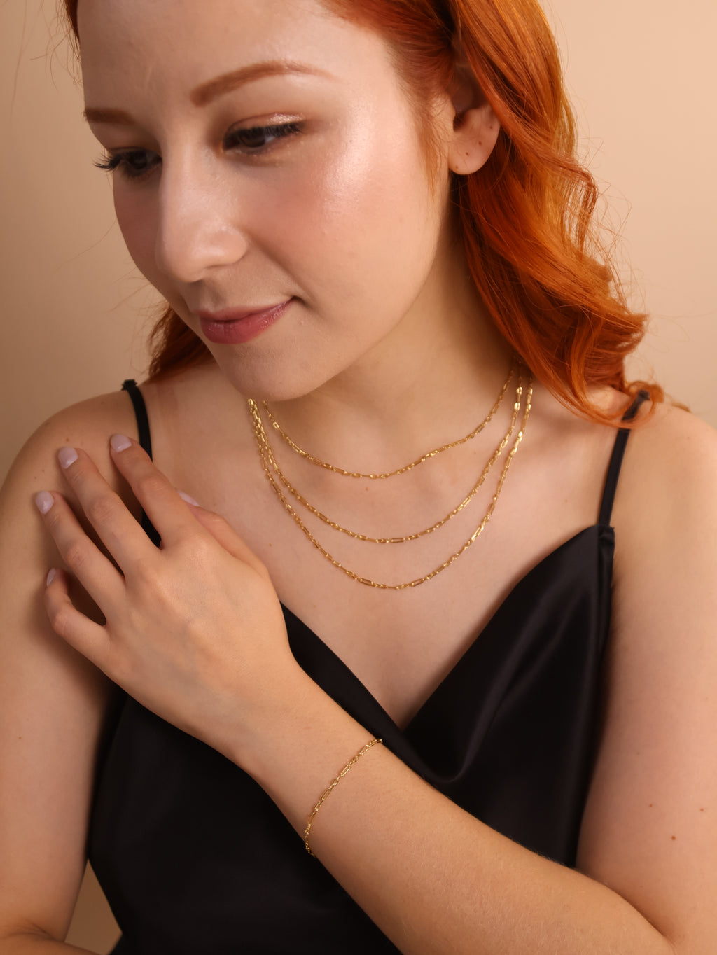 Woman showcasing layered gold necklaces and a bracelet, exuding elegance in a black outfit.