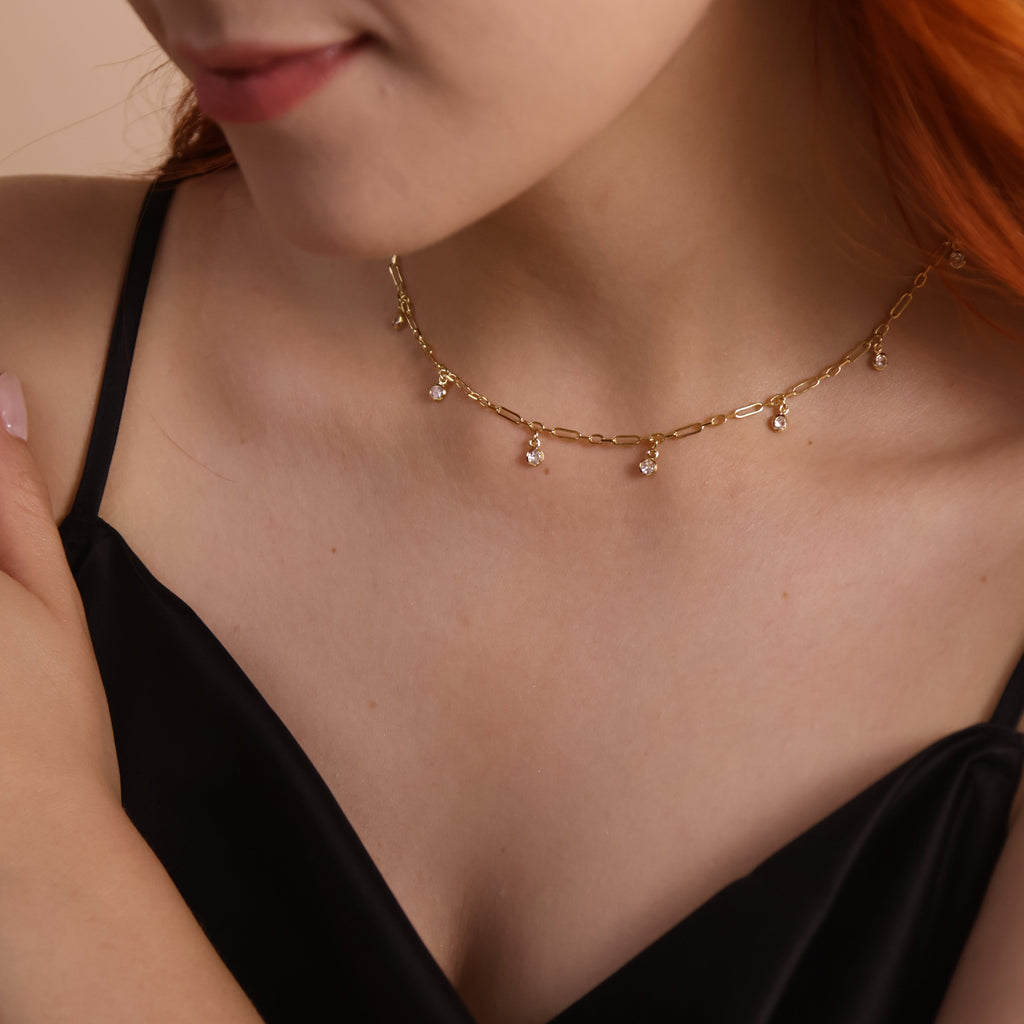 18K gold filled paperclip chain necklace with bezel CZ drops, elegantly displayed on a model's neckline.