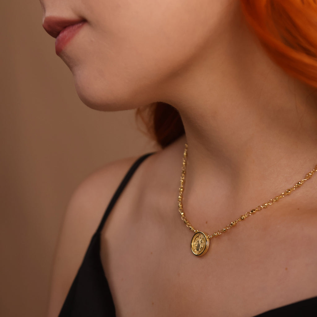 Close-up of a person wearing a gold necklace with a pendant against a neutral background