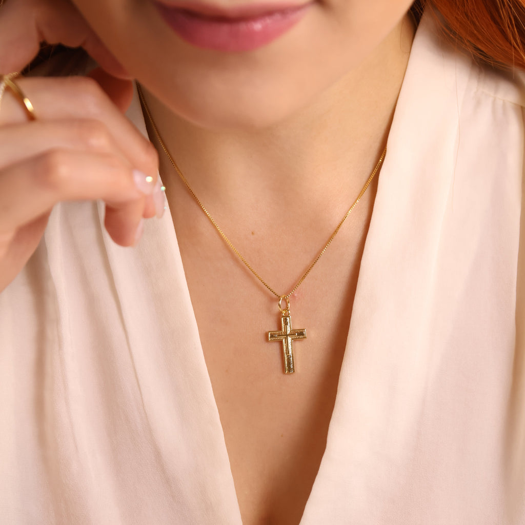 Close-up of a woman wearing a gold necklace with a cross pendant.