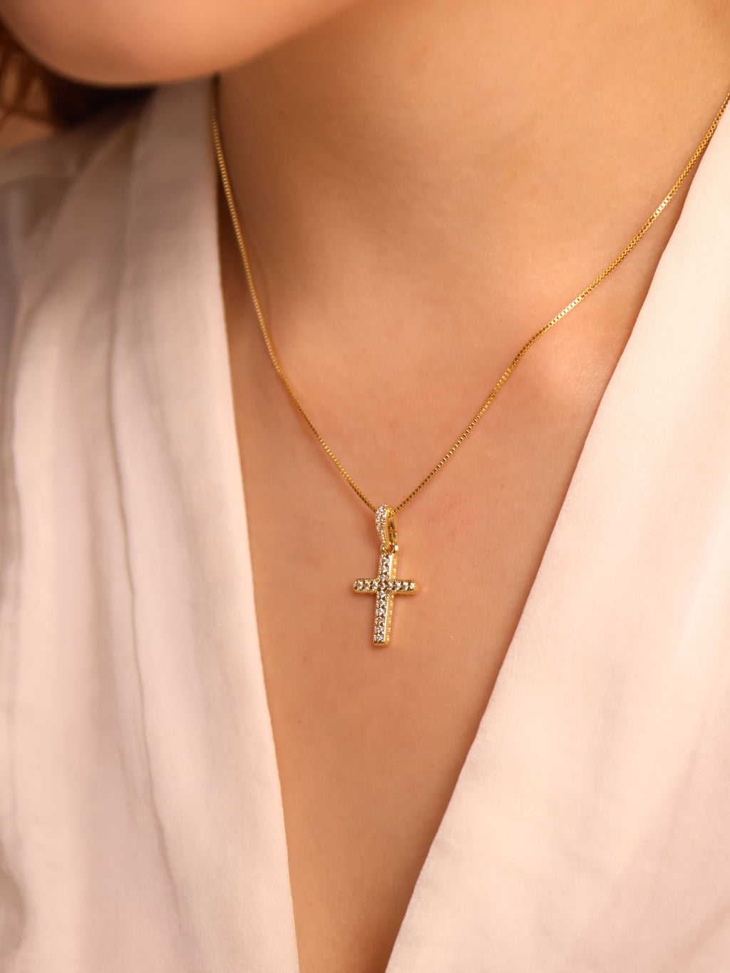 Gold necklace with a cross pendant on a person wearing a light pink top.