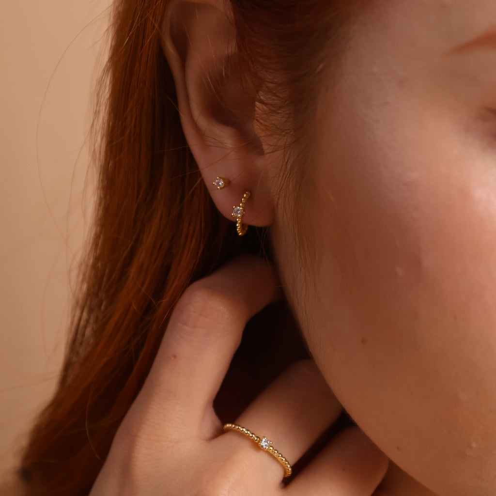 Close-up of a person with red hair wearing gold earrings and a ring on a beige background